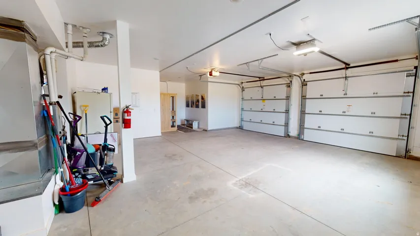 Spacious garage featuring a concrete floor, two white overhead garage doors, exposed ductwork, and fluorescent lighting fixtures