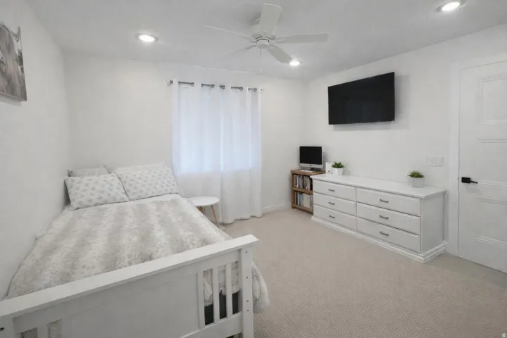 Carpeted room featuring a white ceiling fan with integrated lighting, recessed ceiling lights, and a window with sheer curtains