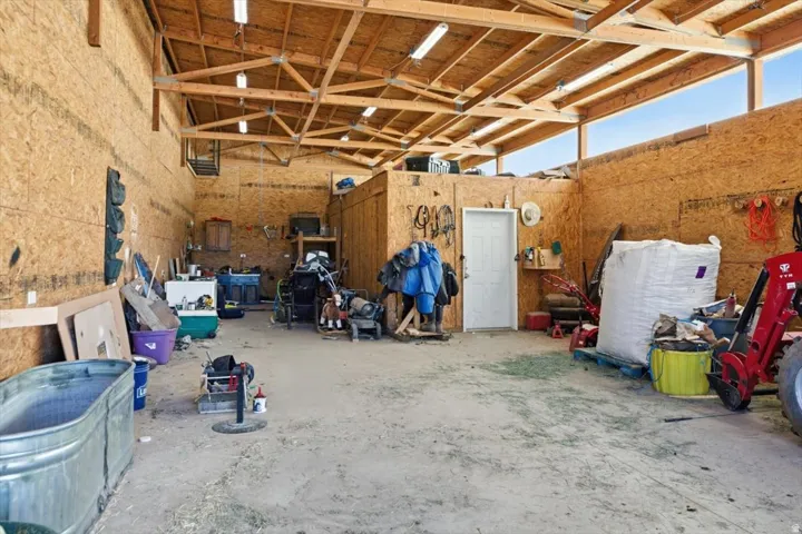 Spacious utility building featuring exposed wood beam ceiling, ample natural light from upper windows, durable OSB wall paneling, and concrete flooring