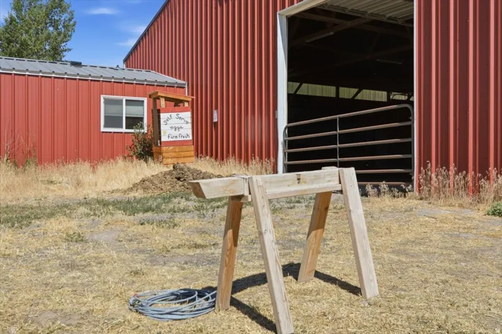 Red metal-sided barn with a gray metal roof, featuring a large open entrance with a metal gate