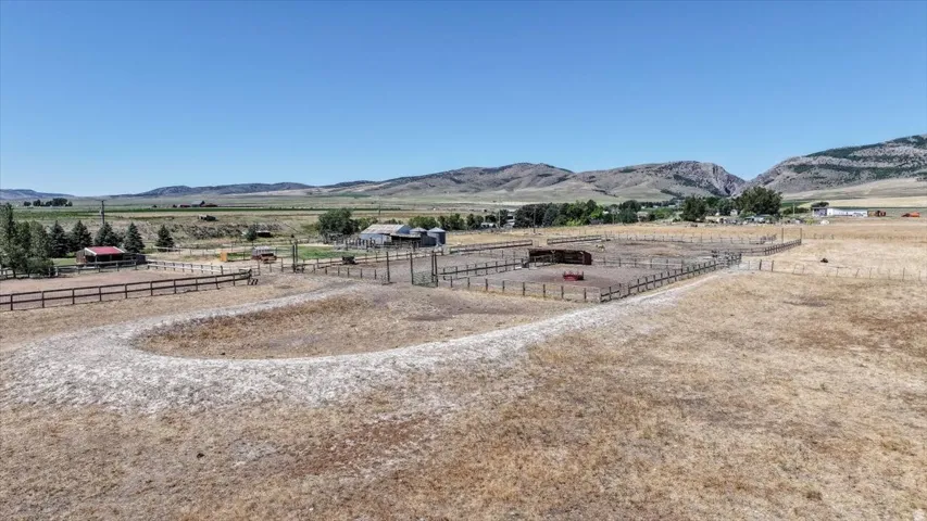 Expansive property featuring a large fenced paddock, additional fenced enclosures, multiple outbuildings, and distant mountainous terrain