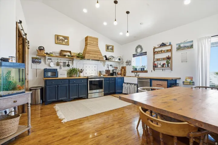 Vaulted ceiling kitchen featuring wood-finish flooring, dark blue cabinetry, stainless steel appliances, a farmhouse sink, and a wooden range hood