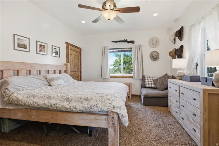 Carpeted bedroom featuring a rustic wood door, ceiling fan with integrated lighting, recessed lighting, and a window with exterior scenery