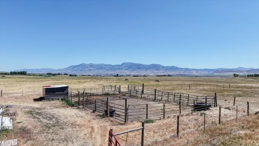 Expansive fenced enclosure with a small shelter on a large rural property, featuring a distant mountain range backdrop