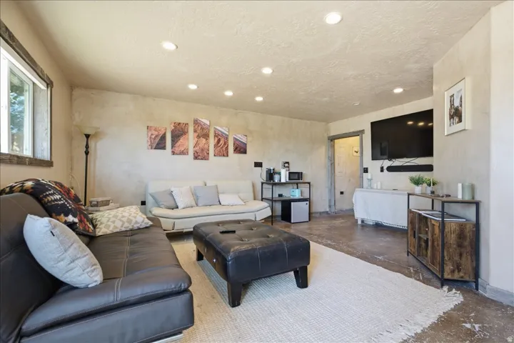 Spacious living area featuring recessed lighting, a window with wood trim, textured walls, concrete flooring, and an open doorway