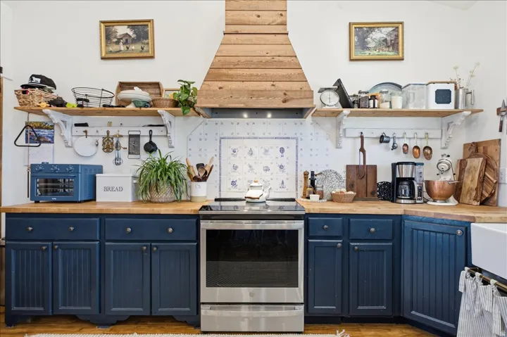Kitchen featuring a stainless steel range, custom wood-finish range hood, blue-and-white patterned backsplash, wood-finish countertops, and blue lower cabinetry