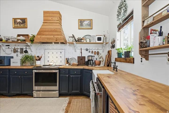Kitchen featuring dark blue cabinetry, butcher block countertops, a stainless steel range, and a wood-paneled range hood