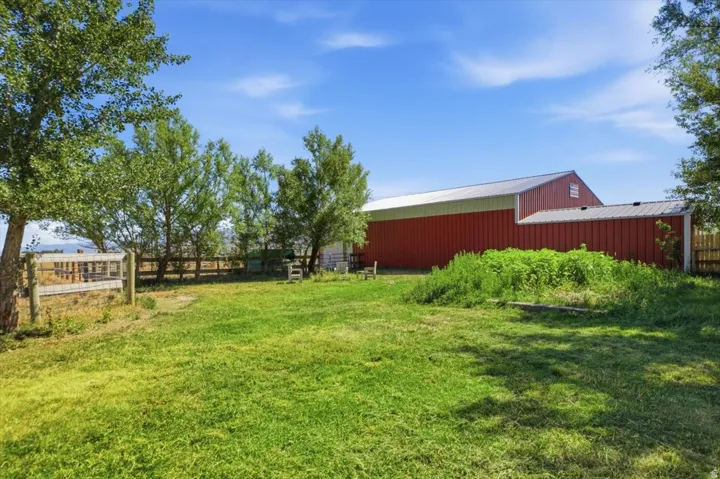 Expansive grassy area with a red barn structure featuring a metal roof and an attached shed