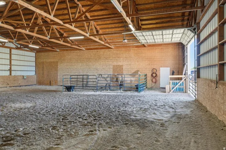 Spacious indoor arena with sand footing, exposed wood beam ceiling, ample fluorescent lighting, and large overhead door entry