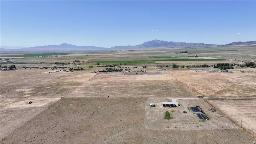 Expansive rural property featuring a main residence with a light-colored roof, multiple outbuildings, and several dark-lined cultivation beds