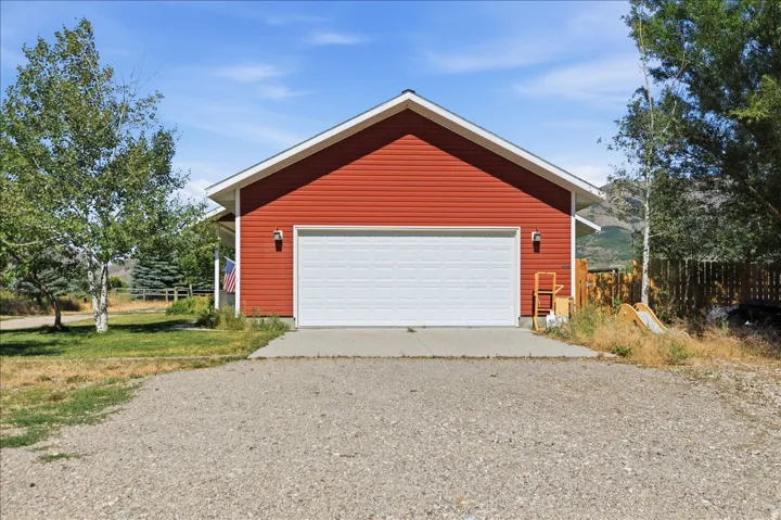 Red horizontal siding exterior with a white garage door, concrete driveway apron, and a gravel surface