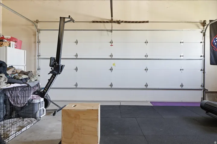 Garage interior featuring concrete flooring, a white sectional garage door, exposed garage door tracks, and a black rubber mat floor section