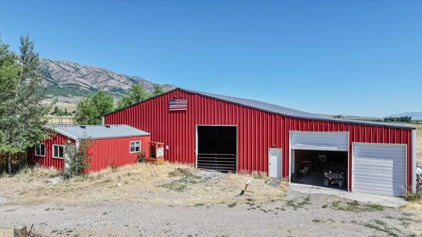 Expansive red metal barn with multiple bays and a separate attached structure, featuring a large open entrance and an overhead door