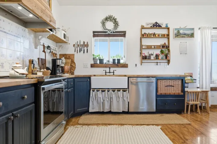 Kitchen featuring a farmhouse sink, stainless steel dishwasher, and wood-finish flooring