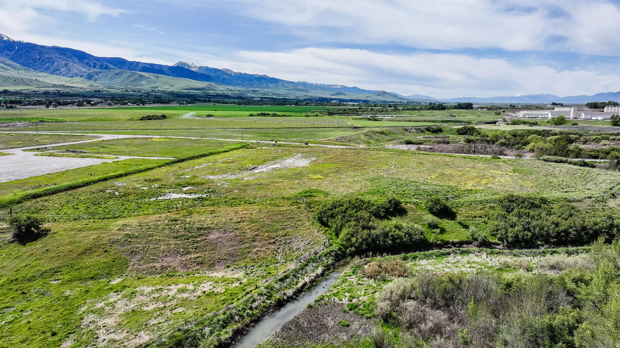 Expansive undeveloped land featuring a meandering stream, varied green vegetation, and distant mountain ranges