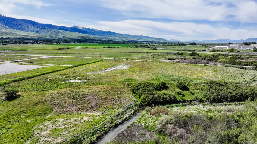 Expansive undeveloped land featuring a meandering stream, varied green vegetation, and distant mountain ranges