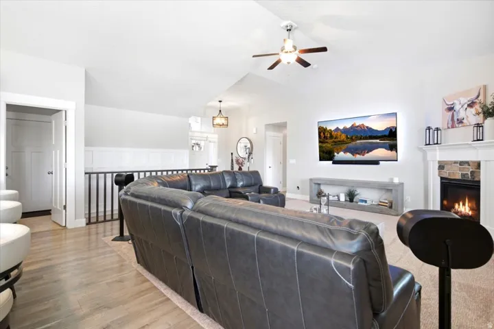Spacious living area featuring a vaulted ceiling with a ceiling fan, a stone-surround fireplace with a white mantel, and wood-finish flooring