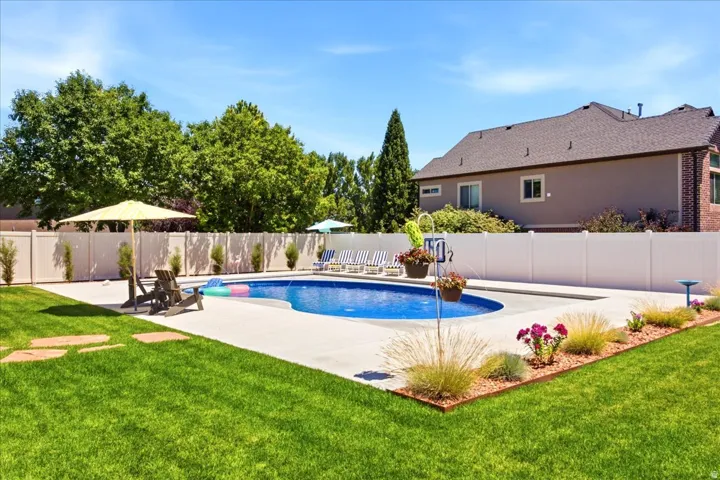 Expansive backyard featuring a curved swimming pool with concrete decking, surrounded by a white privacy fence