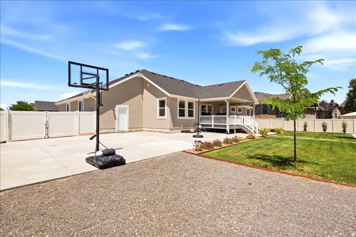 Expansive backyard featuring a covered patio, manicured lawn, gravel area, and white privacy fencing