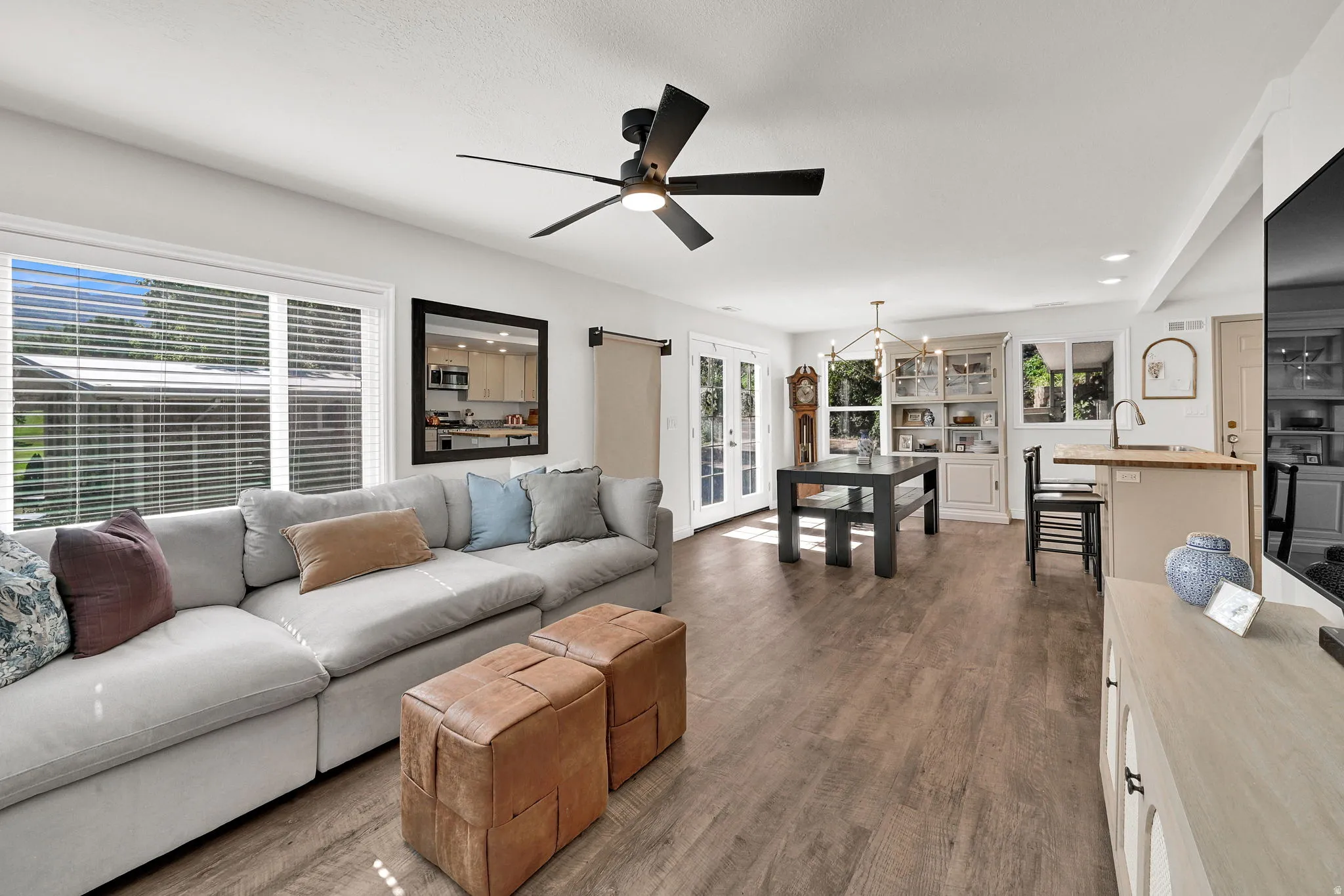 Open-concept living space featuring wood-finish flooring, a contemporary ceiling fan, and large windows with blinds