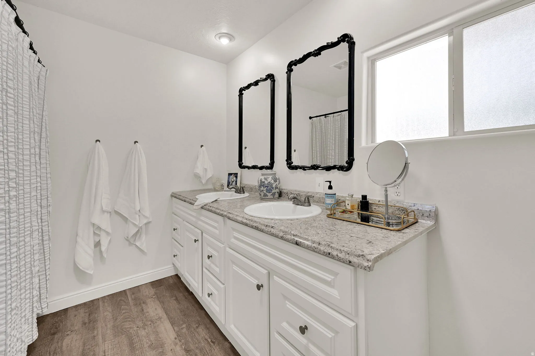 Owners ensuite featuring a dual-sink vanity with a light granite-finish countertop, white cabinetry with dark hardware, and wood-finish flooring