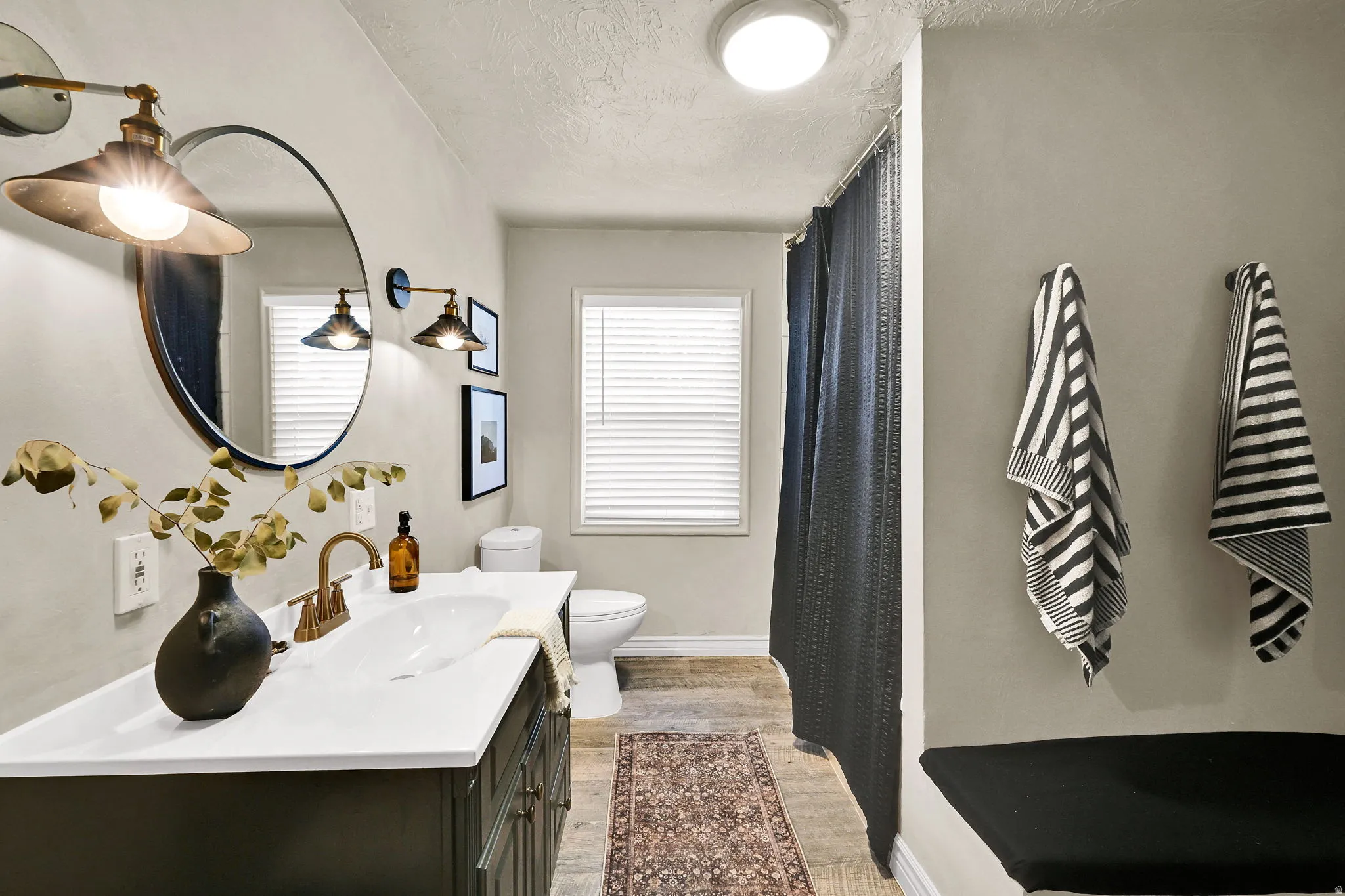 Bathroom featuring a dark vanity with a white countertop, oval sink, and brass-finish faucet, and large tub/shower