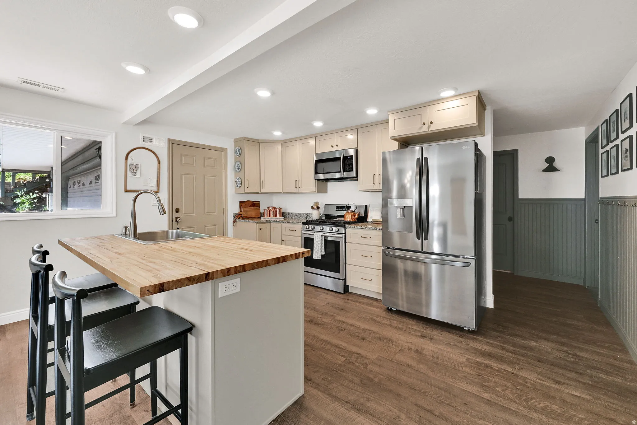 Modern kitchen featuring light wood-finish flooring, stainless steel appliances, neutral cabinetry, recessed lighting, and a butcher block island with integrated sink