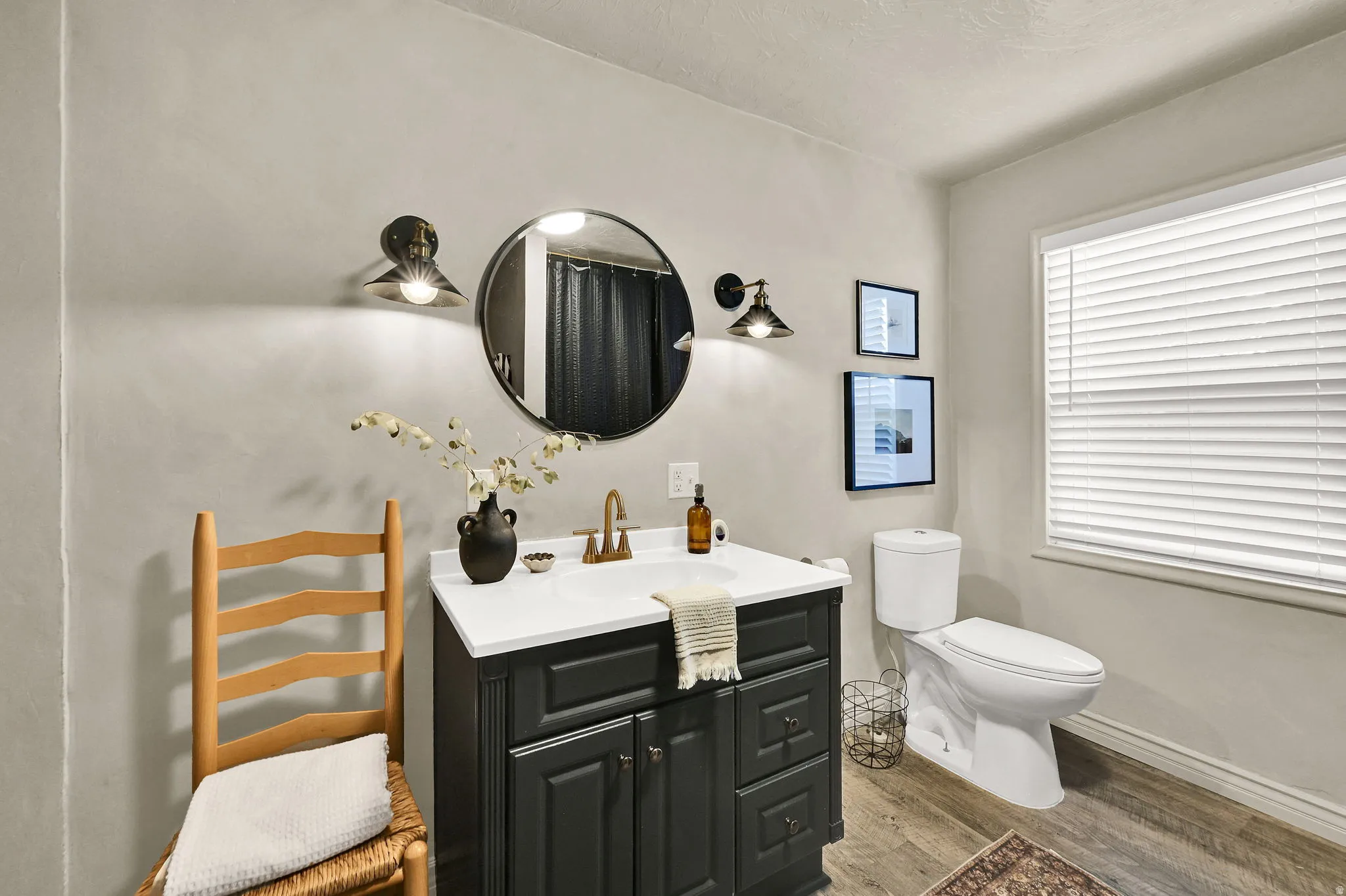 Bathroom featuring a dark wood-finish vanity with a white countertop and brass-finish faucet, a round mirror, and two wall sconces