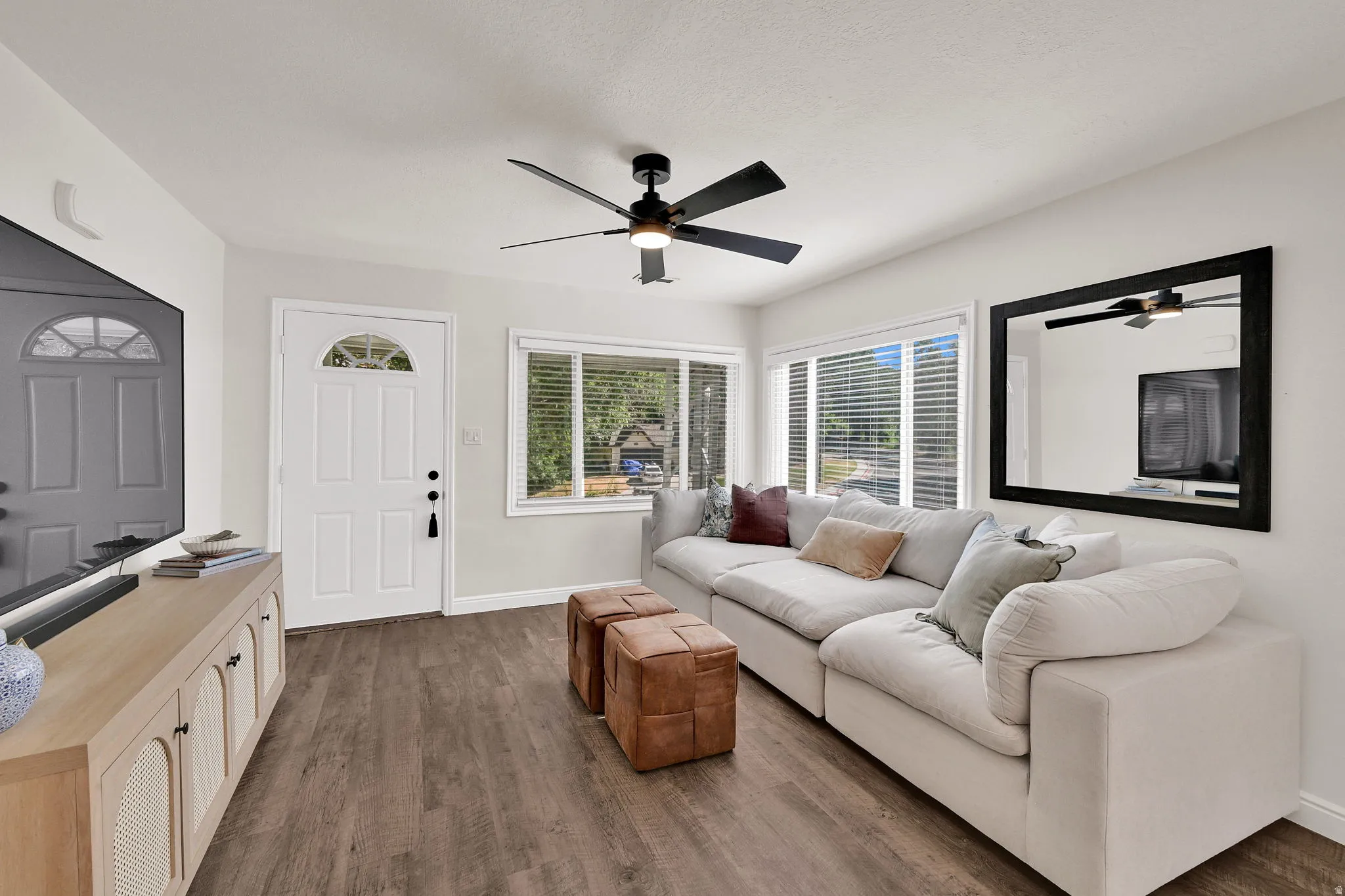 Open living area featuring wood-finish flooring, a contemporary ceiling fan with integrated lighting, and multiple windows providing natural illumination