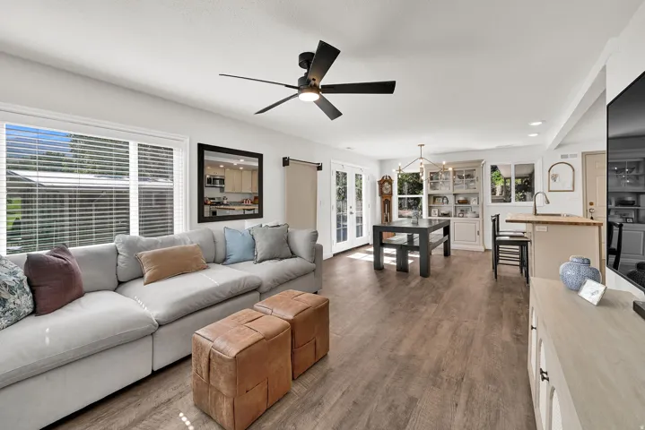 Open-concept living space featuring wood-finish flooring, a contemporary ceiling fan, and large windows with blinds