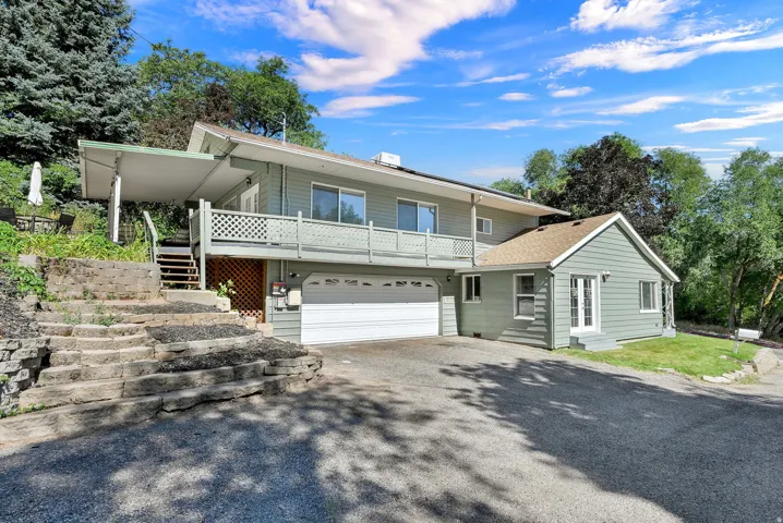 Exterior featuring light green siding, an attached two car garage, a covered second-story balcony with lattice railing, and a side entrance with double doors
