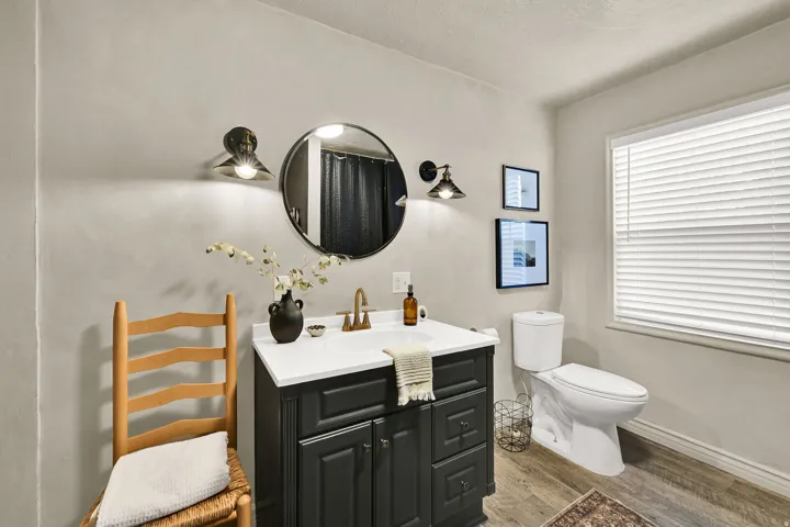 Bathroom featuring a dark wood-finish vanity with a white countertop and brass-finish faucet, a round mirror, and two wall sconces
