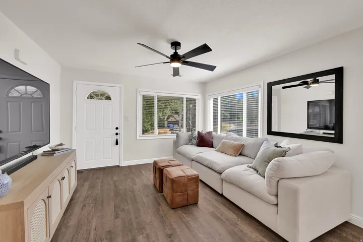 Open living area featuring wood-finish flooring, a contemporary ceiling fan with integrated lighting, and multiple windows providing natural illumination