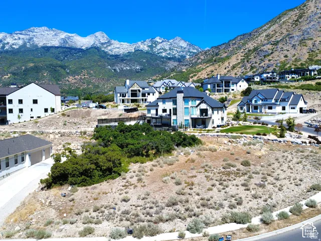 Mountainous terrain with residential development featuring a newly constructed white stucco home with dark roofing, multiple balconies, and a manicured lawn