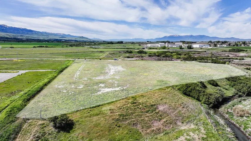 Expansive undeveloped land parcel featuring a natural water channel, distant mountain ranges, and varied topography