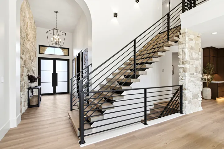 Entryway featuring a floating staircase with black metal railings, a stone accent wall, wood-finish flooring, a contemporary chandelier, and double entry doors with frosted glass panels and an arched transom window