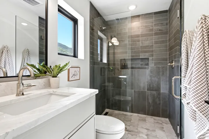 Walk-in shower with dark gray rectangular tile surround, glass enclosure, and built-in niche