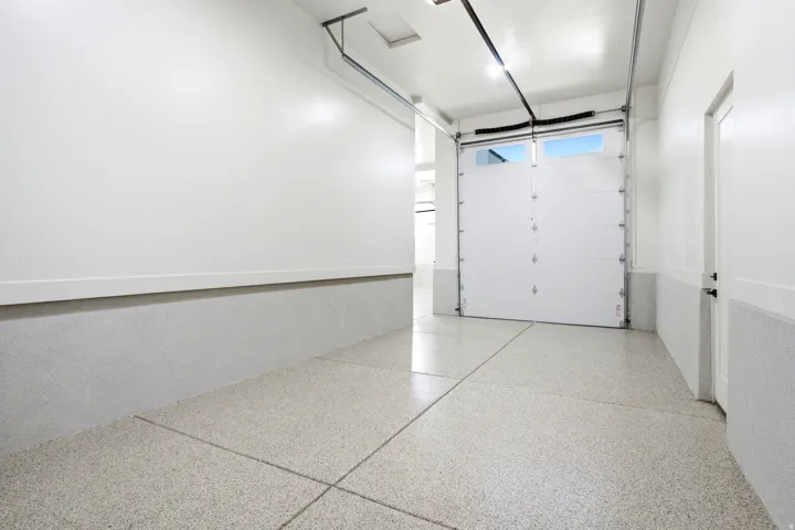 Garage interior featuring an epoxy coated floor, white paneled garage door with upper windows, and recessed lighting