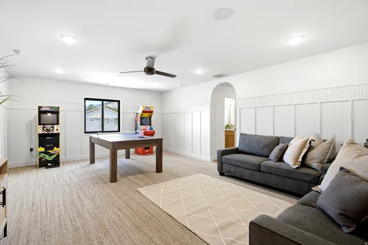 Spacious room featuring broadloom carpet flooring, wainscoting with board and batten detailing, and an arched doorway