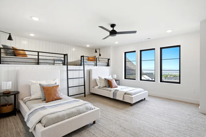 Spacious room featuring multiple sleeping areas, three tall windows with black frames, white vertical shiplap paneling, recessed lighting, and a ceiling fan