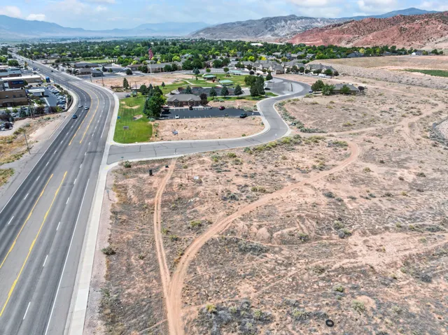 Expansive undeveloped land featuring a paved roadway, concrete curb, and gravel terrain with distant mountainous formations
