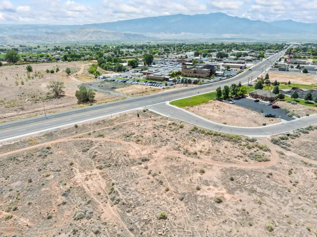 Expansive undeveloped terrain featuring a curving paved road, surrounding commercial and residential buildings, and distant mountains