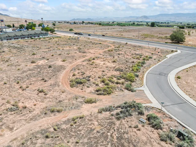 Expansive undeveloped land featuring a paved road with curbs, established utility boxes, and distant mountain backdrops