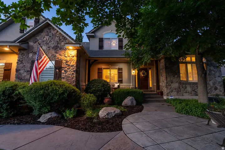 Stone facade home featuring mature landscaping, a concrete paver walkway, plantation shutters, and a covered entryway with an ornate front door