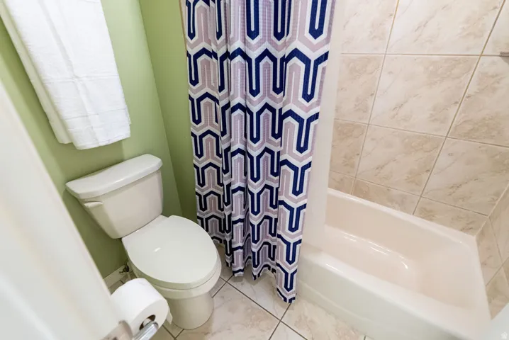 Bathroom featuring a full bathtub with light-toned tile surround, ceramic tile flooring, and a standard toilet