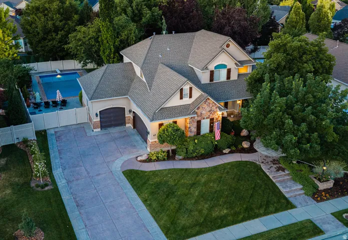 Stucco and stone facade property featuring an attached two-car garage, mature landscaping, and a fenced backyard swimming pool