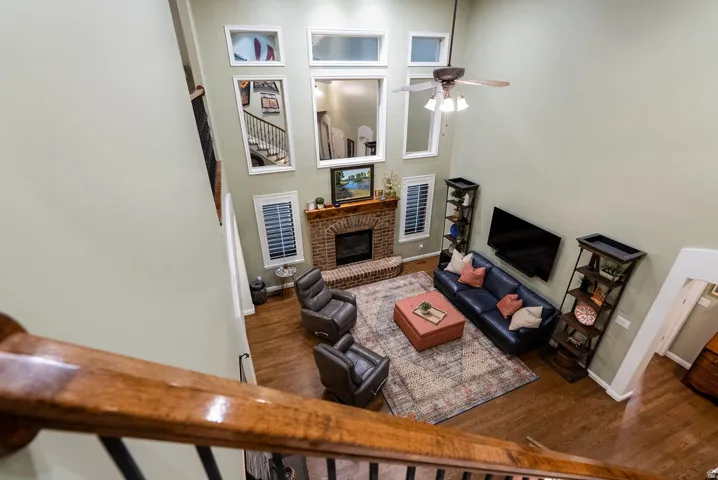 Two-story living area featuring a brick fireplace with a wood mantle, hardwood flooring, and a ceiling fan