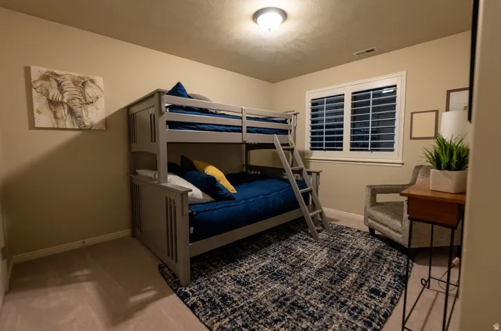 Carpeted interior room featuring light beige walls and a single window with white plantation shutters