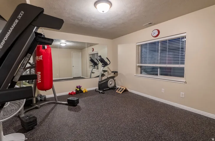 Dedicated fitness space featuring specialized rubberized flooring, a full-wall mirror, and a window with horizontal blinds