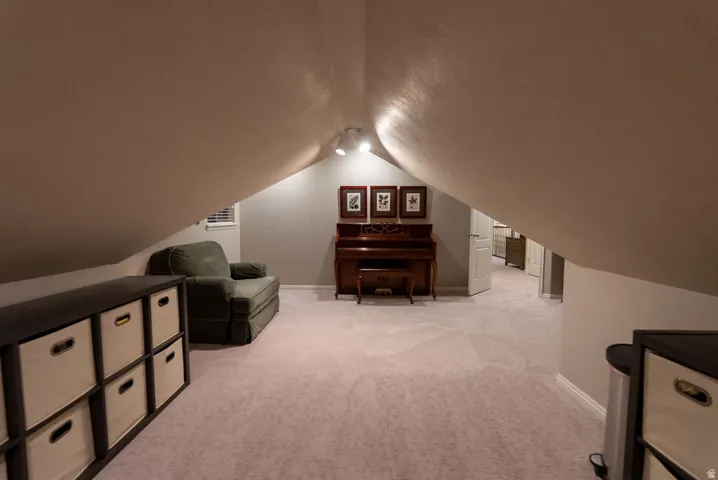 Carpeted attic space featuring sloped ceilings, track lighting, and a white interior door